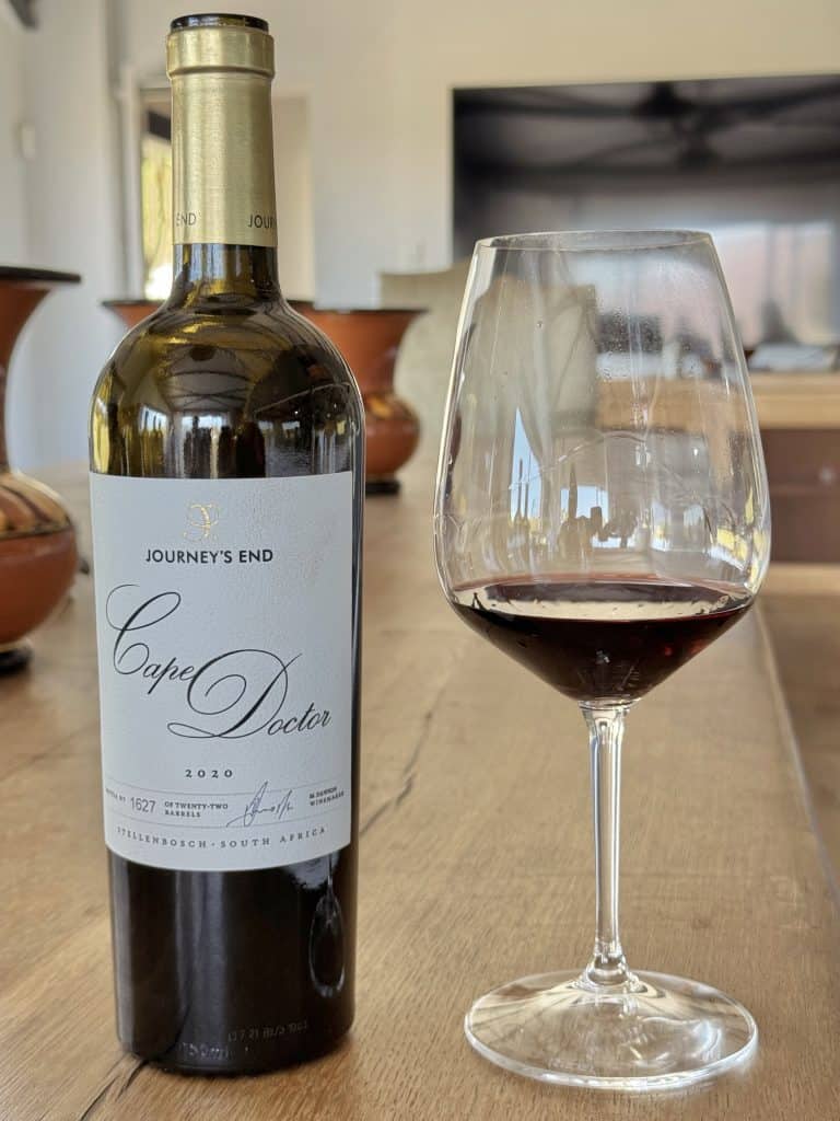 Rich red wine in a wine glass on a wooden table, with a bottle labelled "Cape Doctor," showcasing a South African wine selection from Swirl and Spice, perfect for wine tasting and pairing.