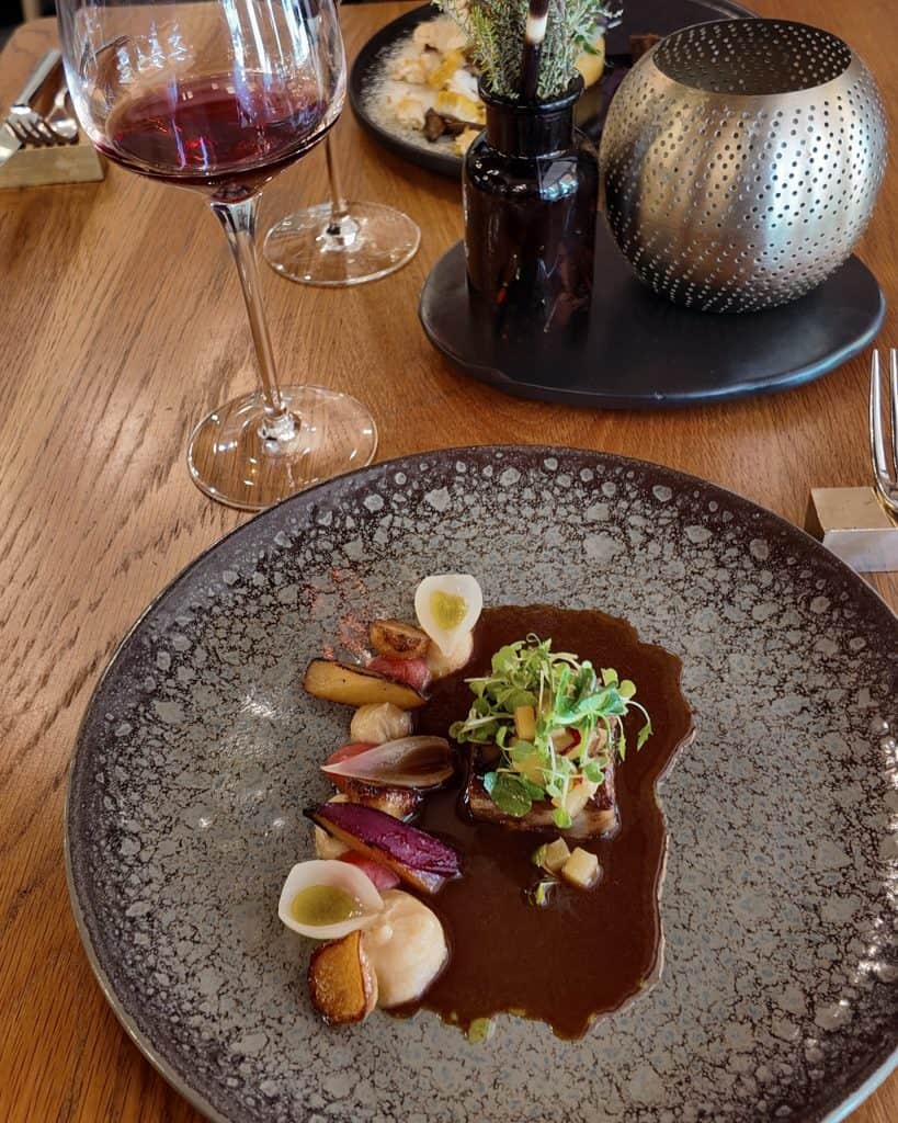 Elegant plated beef tenderloin dish with rich sauce, garnished with microgreens and roasted vegetables, served on a stylish black plate at a fine dining restaurant.