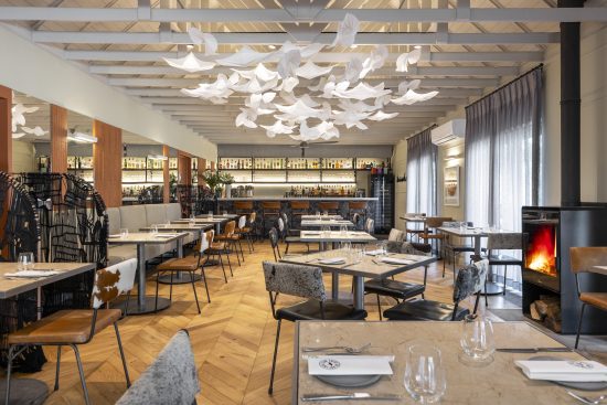 Spacious restaurant dining area featuring modern furniture, decorative lighting, and a cozy fireplace, perfect for a relaxing dining experience.