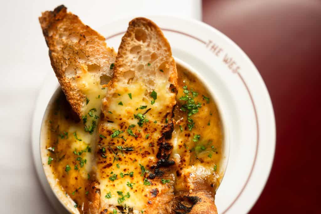 Close-up of a baked fish fillet with melted cheese and herbs, served with toasted bread slices in a white bowl.