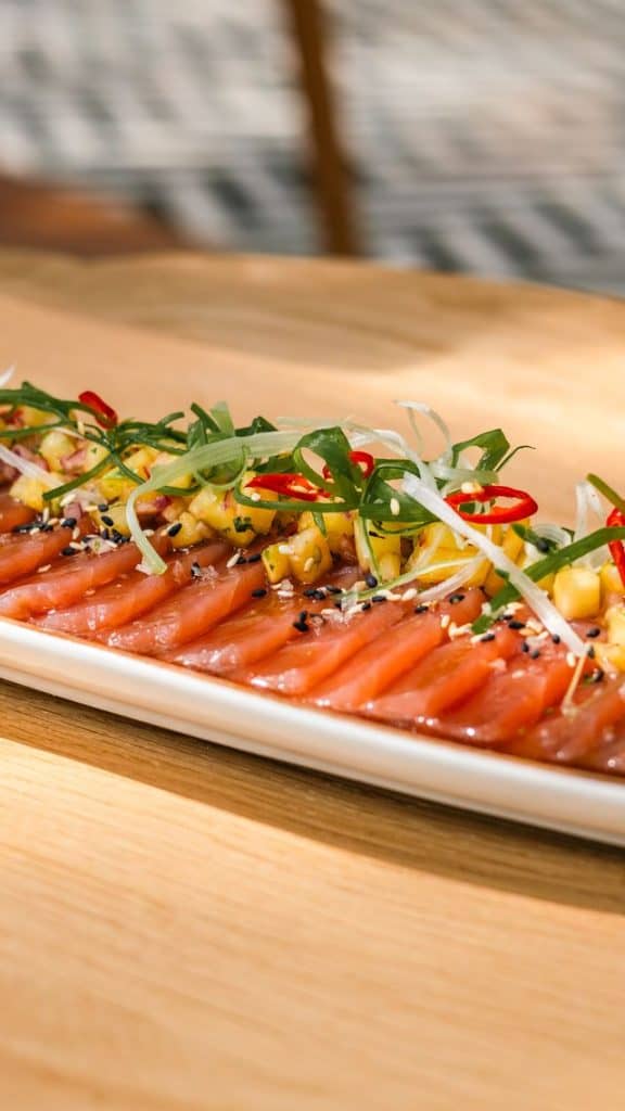 Close-up of a fresh salmon sashimi platter garnished with chili, green onions, and sesame seeds on a white plate.