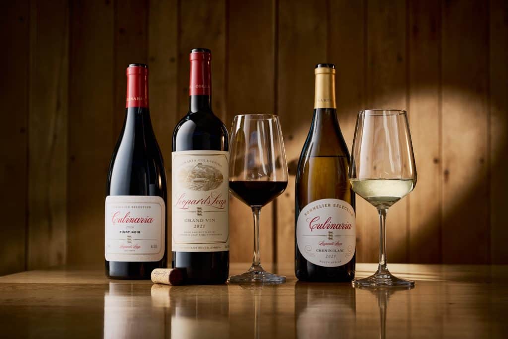 Two bottles of red wine and two glasses of wine, one red and one white, on a wooden surface with a wooden background.