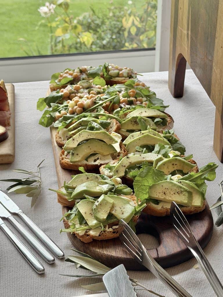 Assorted open-faced avocado and chickpea sandwiches on a wooden serving board with fresh greens.