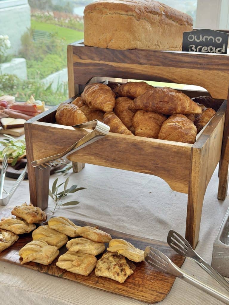 Fresh baked bread and pastries displayed on a wooden stand and tray at a breakfast buffet.