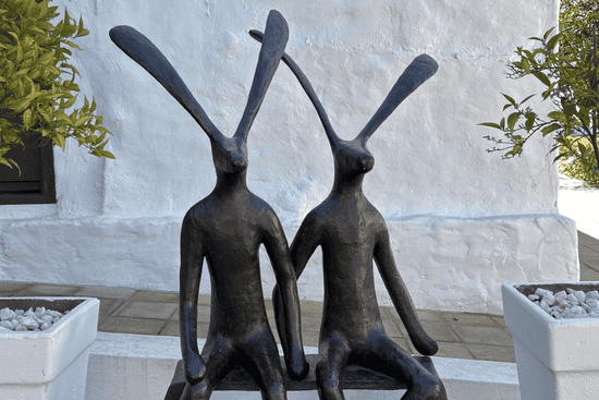Artistic sculpture of two seated rabbits outside Hazendal Wine Estate in Stellenbosch, with white walls and potted plants.