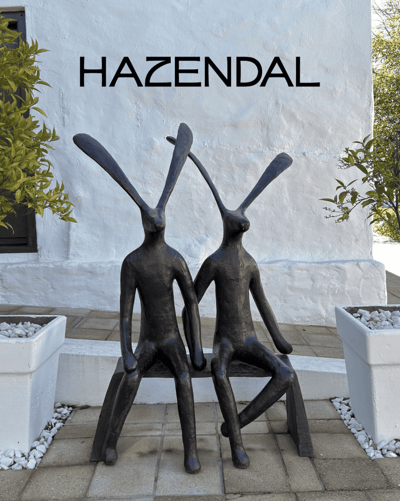 Artistic sculpture of two seated rabbits outside Hazendal Wine Estate in Stellenbosch, with white walls and potted plants.