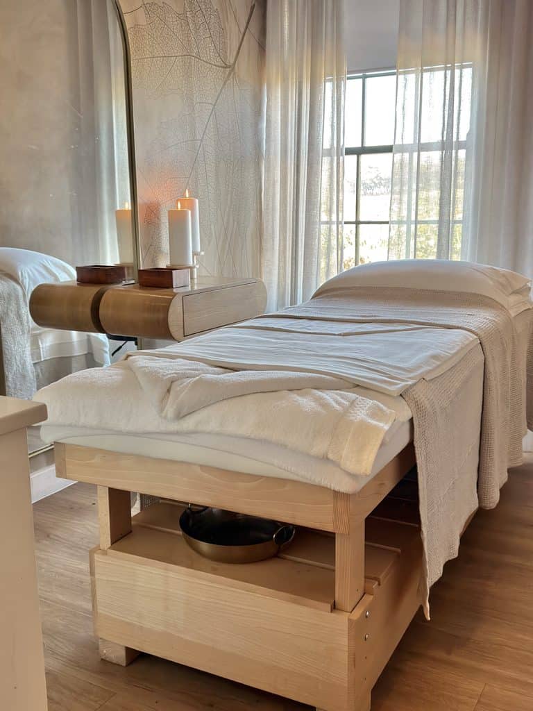 Relaxing massage room with a massage table, candles, and natural light from large windows.