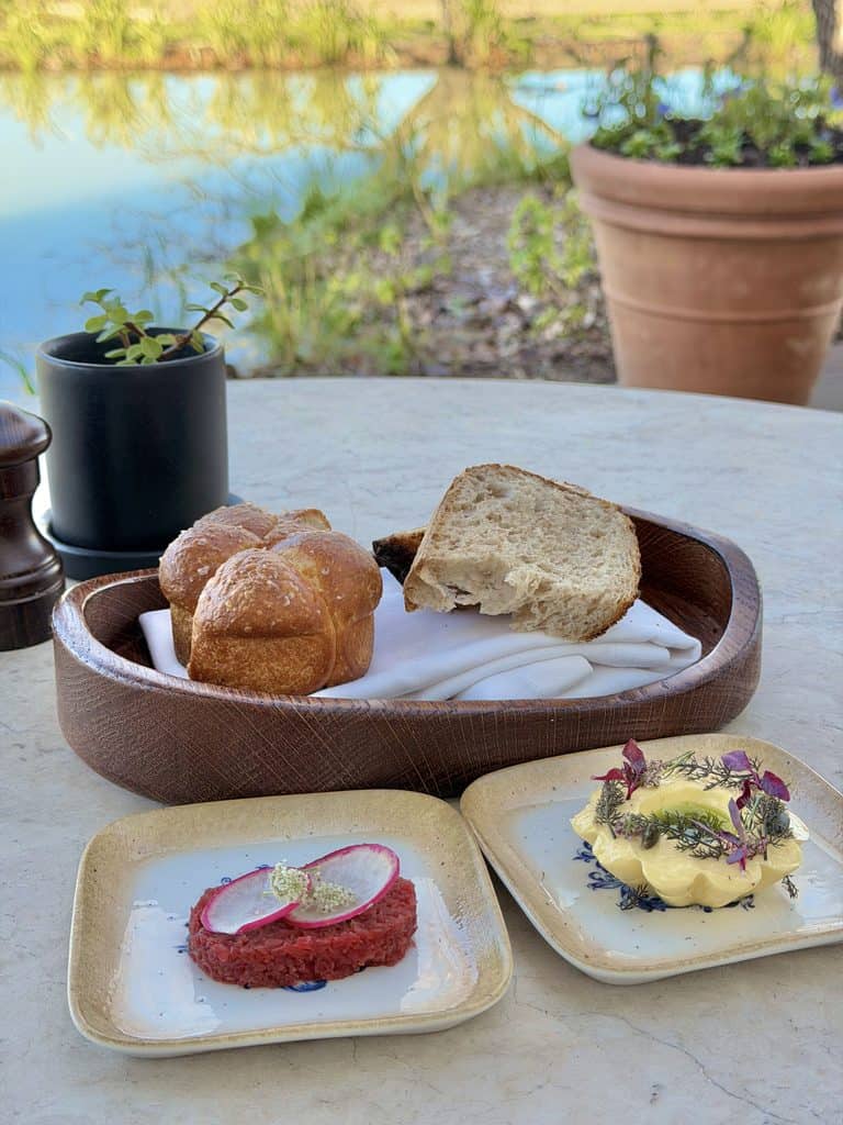 Delicious bread rolls and gourmet dishes at Hazendal Wine Estate with a scenic lake view in the background.