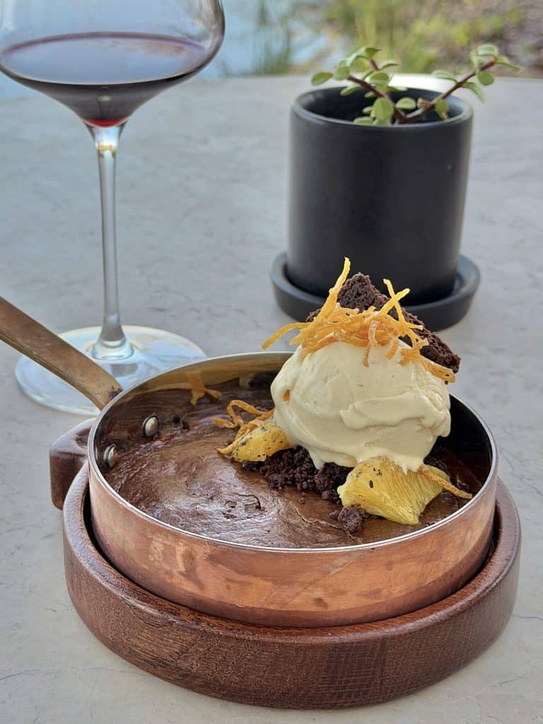 Decadent chocolate dessert with vanilla ice cream, garnished with orange zest and chocolate pieces, served with a glass of red wine on a table.
