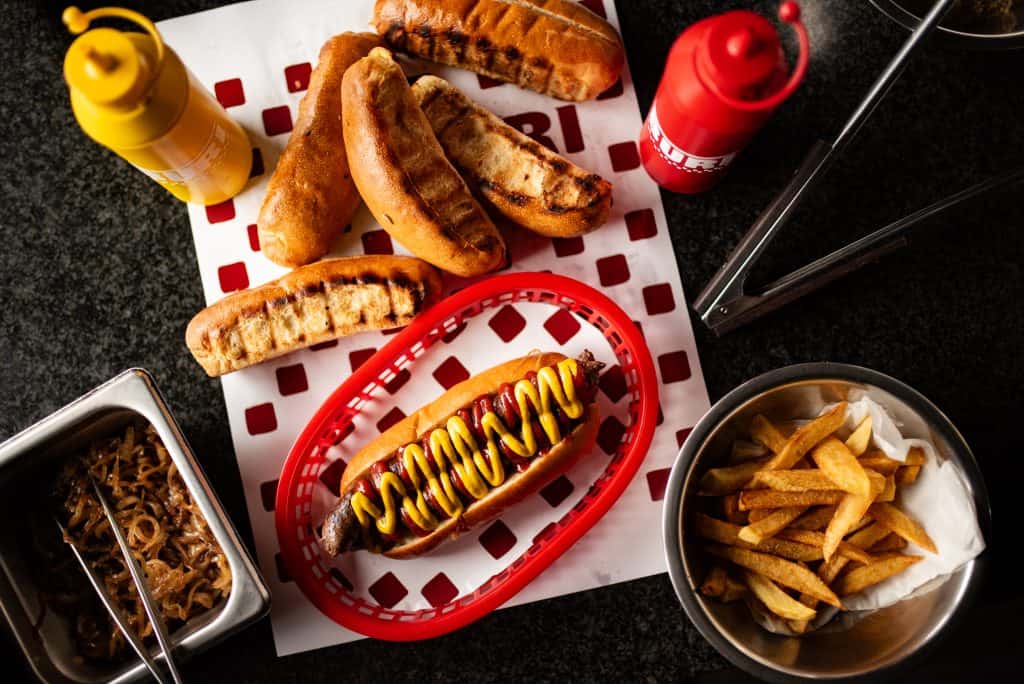 Traditional South African boerewors sausage with mustard and ketchup, served with fries and grilled chicken wings on a black table.