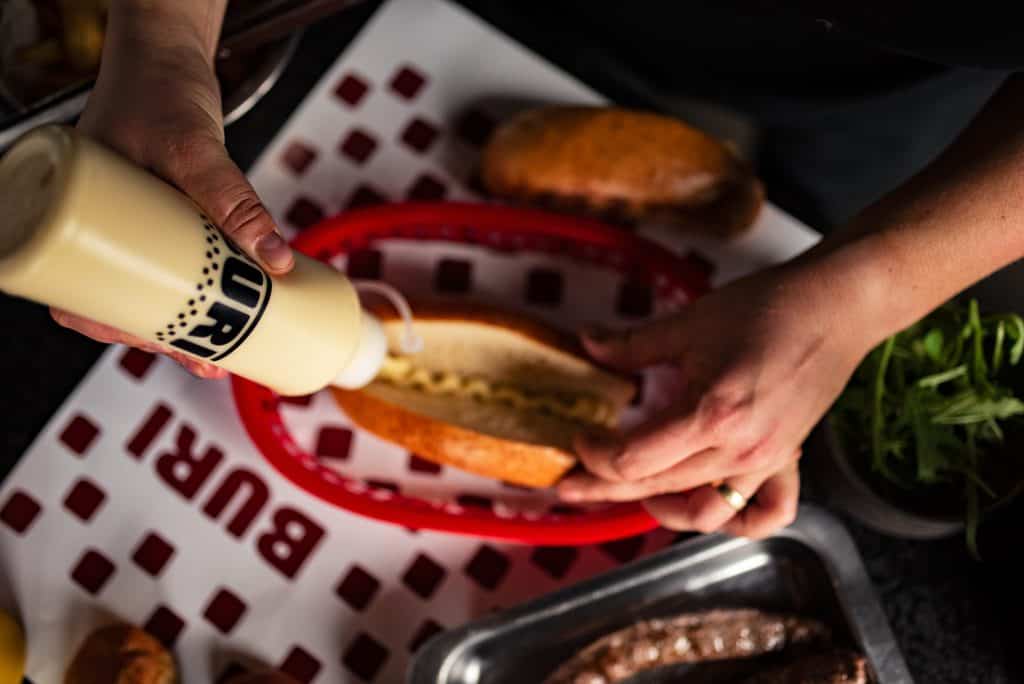 Person adding mustard to a burger at Buri restaurant during a South African celebration.